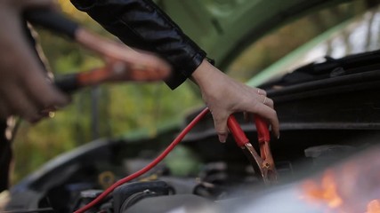 Close-up shot of a girl attaching jumper cables to a battery. Jump Starting a car, detail footage of cables charging a dead battery