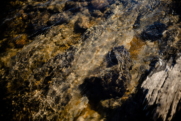 Stone beneath serene river water, river water waves brushing through the stones fresh water stream in mountain brook, close up