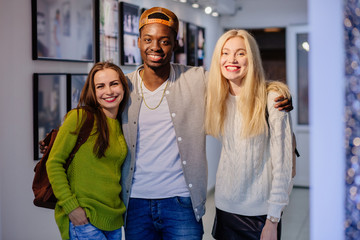 Team of three happy multi ethnic students, friends, one black man and two european women hugging...
