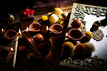 Diwali diya or lighting in the night with gifts, flowers over moody background. Selective focus