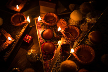 Diwali diya or lighting in the night with gifts, flowers over moody background. Selective focus