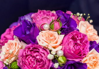 wedding rings on top of a pearl on a bride's bouquet of peony roses of pink, cream and purple colors