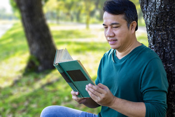 Male reading a textbook with smiling face enjoying in the park. The concept of reading make happy all genders and all ages.
