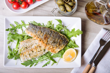 Grilled seabass fillet with arugula, lemon, tomatoes and capers. Close-up.