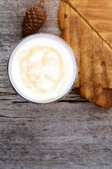 Cup of latte with leaf and pine cone on wooden table, top view image