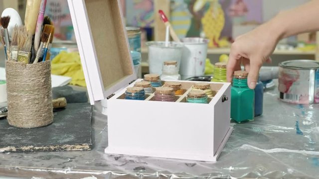 Hands of fingering the jar and bottles of paint, picking the right color in the vases