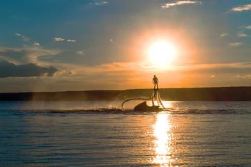 Fotobehang Silhouette of a fly board rider  over a river against the setting sun.  © twinlynx