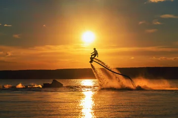 Fototapete Sport Silhouette eines Flyboard-Fahrers über einem Fluss gegen die untergehende Sonne.