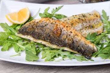 Grilled seabass fillet with arugula and lemon. Close-up.