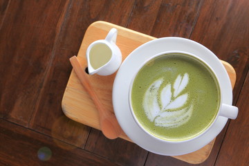 White cup of matcha green tea latte art with foam on natural board over rustic wooden table with copy space