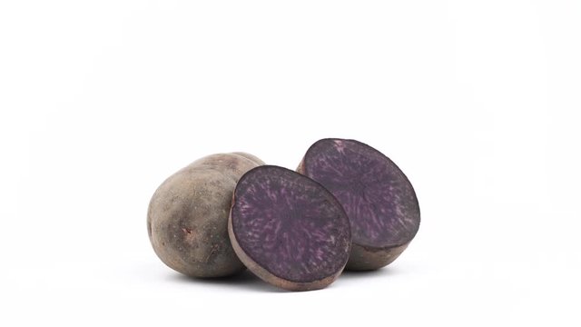 One whole noire potato, one half of violet potato and one slice. Slowly rotating on the turntable isolated on the white background. Close up. Macro.