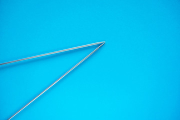 Long iron knitting needles on light blue background.