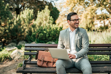 Happy young business man sitting on the bench with laptop.
