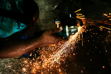 Close-up image of worker cutting metal with a grinder. Sparks flying.