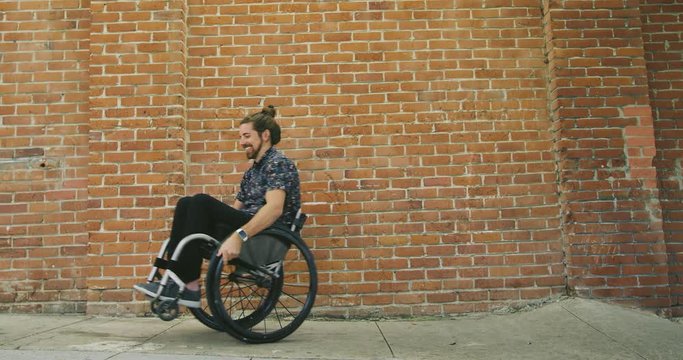 Young happy disabled man dancing and spinning in wheelchair in front of brick wall 
