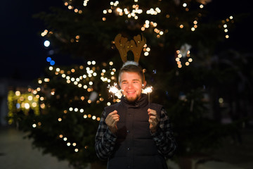 People, holidays and Christmas concept - young funny man in christmas deer costume with bengals light outdoors