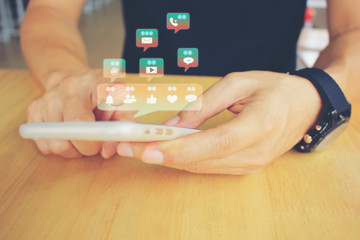 Man hand holding smart phone with hologram or icon of set of social media on the wooden table in restaurant, Communication technology and Social media concept