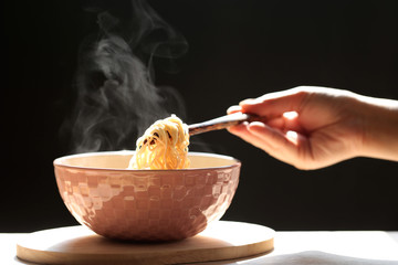 Woman hand holding chopsticks of instant noodles in cup with smoke rising dark background, Sodium diet high risk kidney failure, Healthy eating concept