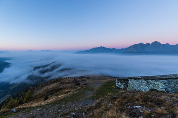 Fototapeta na wymiar Colorful Early Morning Autumn Mountain Panorama View From Mt. Mohar In Nationalpark Hohe Tauern Carinthia To Schober Group and Grossglockner With Fog Down Above The Valley