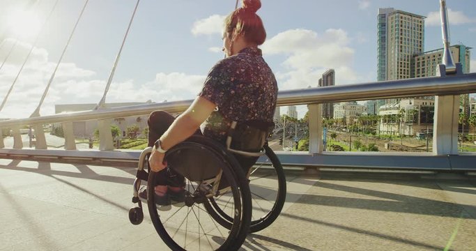 Young Happy Disabled Doing Wheelie In Wheelchair Across Bridge In City With Lens Flare