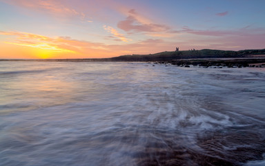 Sunrise over Dunstanburgh Castle on the coast of Northumberland, England, UK.