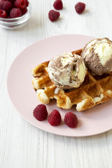 Traditional belgian waffle with icecream  and raspberries on pink plate, side view. White wooden table. Close-up.