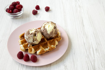 Traditional belgian waffle with icecream and raspberries on pink plate, side view. White wooden background. Copy space.