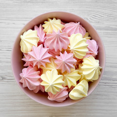 Mini meringues in a pink bowl over white wooden surface, view from above. Flat lay, overhead, top view.