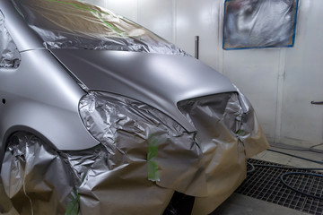 Full painting of a silver car in the back of a hatchback, some parts of which are protected by paper from splashes of paint droplets in a car body repair shop with a special box and equipment