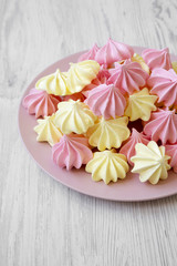 Mini meringues on pink plate over white wooden background, low angle view.