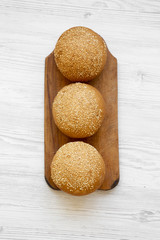 Fresh burger buns with sesame seeds on wooden board on white wooden background, overhead view. Close-up.