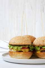 Cheeseburgers on grey plate over white wooden background. Side view. Close-up.