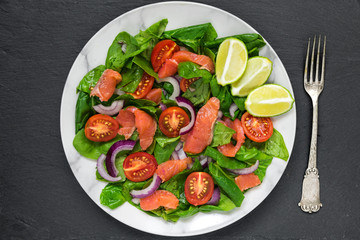 fresh salad with salmon, spinach, cherry tomatoes, red onion and basil in marble plate with fork. healthy food concept