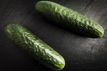 two whole green cucumbers on a black slate table
