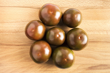 group of dark red kumato tomatoes on a wooden table
