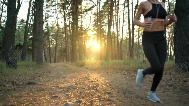 Close up of woman with headphones running through an autumn forest at sunset. Filmed at different speeds - normal and slow motion