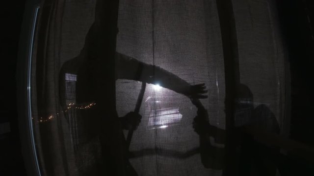 Shadows of two persons on balcony. Guy pointing gun at partner, joking. Another guy picking lock, using scrap. Indoors. Night time. Darkness.