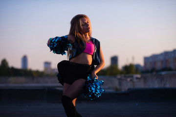 cheerleader with pompoms dancing outdoors on the roof at sunset