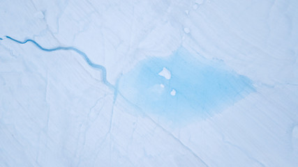 Aerial view from a drone flying over a frozen glacier with a small melt water lake on top. Disko...