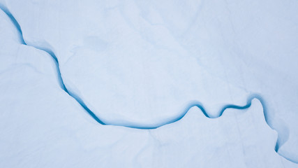 Aerial view from a drone flying over a frozen glacier with a small melt water lake on top. Disko...