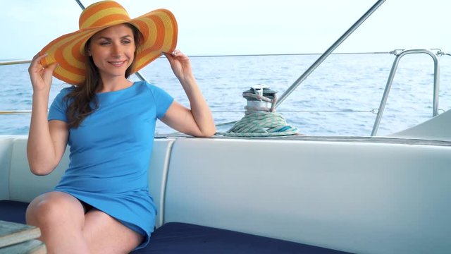 Woman in a yellow hat and blue dress girl rests aboard a yacht on summer season at ocean