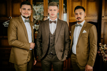 stylish groomsmen helping happy groom getting ready in the morning for wedding ceremony. luxury man in suit in room. Groom preparation before wedding ceremony.