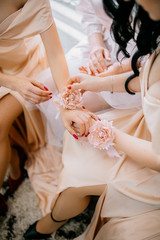 Bridesmaids helping slender bride lacing her wedding white dress, buttoning on delicate lace pattern with fluffy skirt on waist. Morning bridal preparation details newlyweds. Wedding day moments.