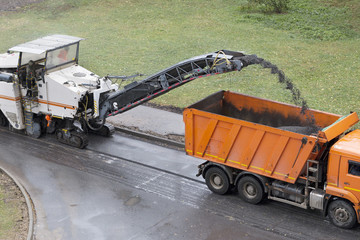 Road milling machine removes old asphalt and loads milled asphalt into the dump truck. Road repair process. High angle view