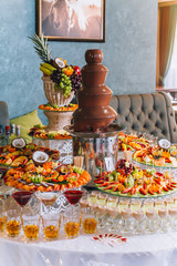 Candy bar with a lot of cookies and fruits during the wedding. chocolate fountain and wedding cake. Coktails and drink at the table