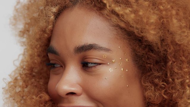closeup womans eyes with golden stars makeup on ideal skin looking at camera and smiling