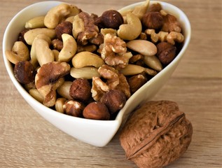 walnuts, whole, and peeled different nuts, cashews, hazelnuts, almonds in a white cup on a wooden table