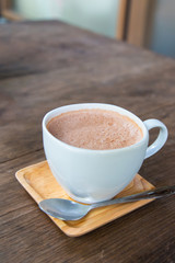Hot cocoa in a white cup on a saucer made of wood.