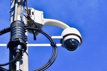 A round-shaped video surveillance camera mounted on a lighting post. Equipment on a blue sky background