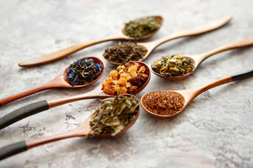 Virious kinds of tea in wooden spoons placed on stone table